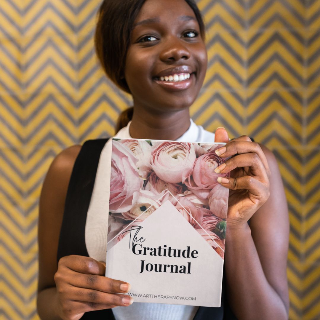 A young black lady holding a book called the gratitude journal.