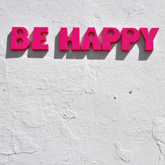 Be happy, made from red plastic letters and stuck on a white rough plastered wall.