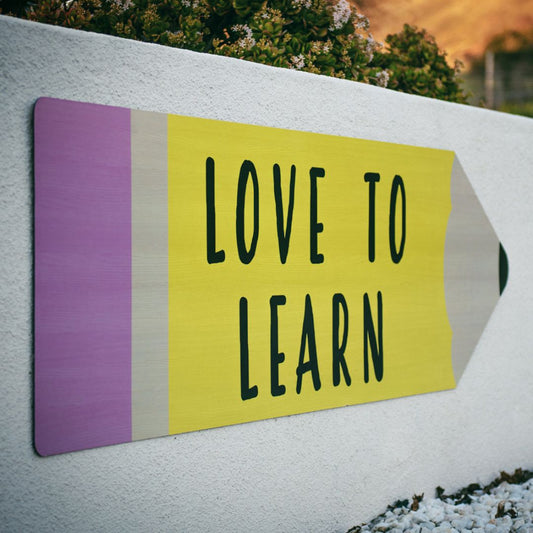 A direction sign in the shape of a pencil with different colours and the words love to learn.