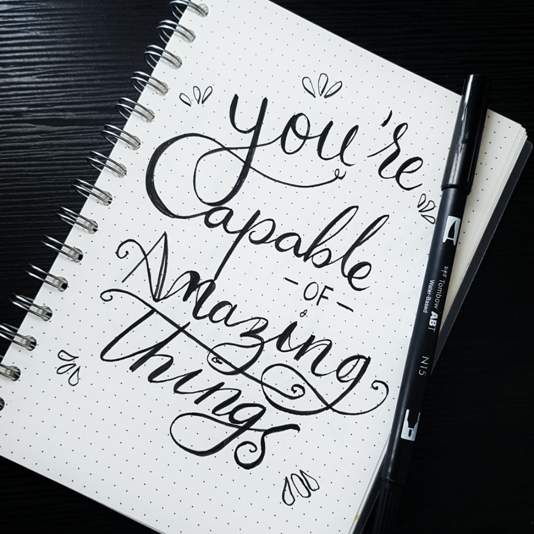 The words, you're capable of amazing things, are written creatively in black ink on white paper.