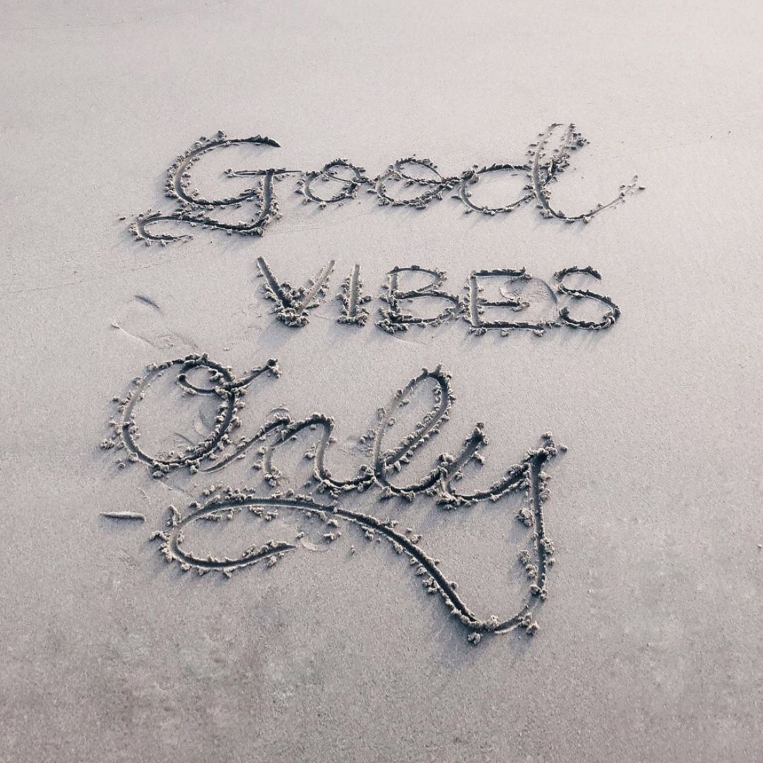 The words "Good Vibes Only" are inscribed on a sandy beach shore