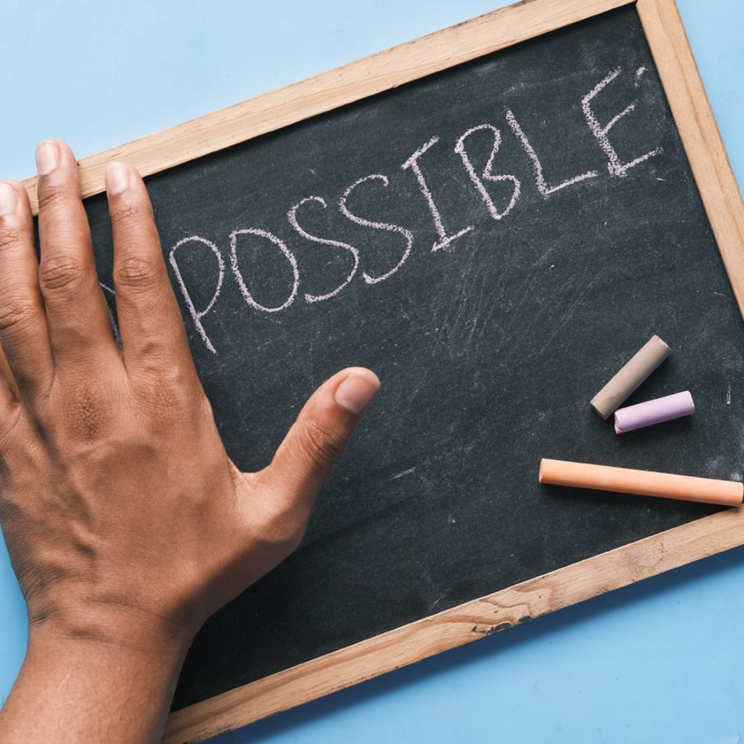 A black hand on a mini chalk board with the word possible written in chalk.